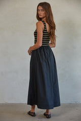 woman wearing a black and striped sleeveless maxi dress with a fitted top and full skirt, standing with her back to the camera