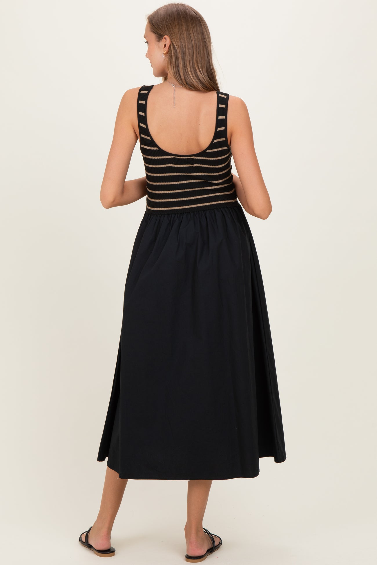 woman wearing a black and striped maternity maxi dress, showing a fitted top and flowing skirt from the back