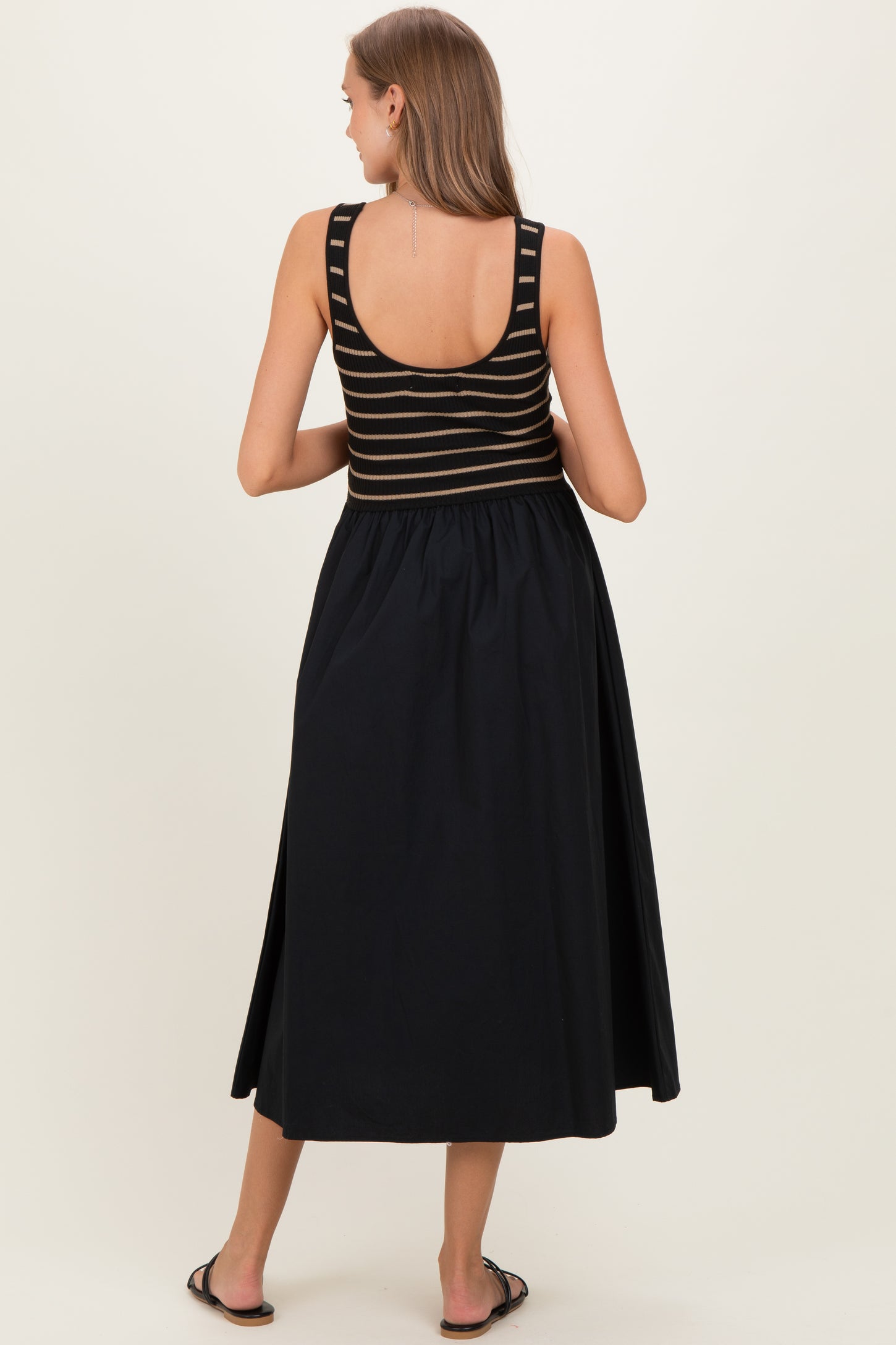 woman wearing a black and striped maternity maxi dress, showing a fitted top and flowing skirt from the back