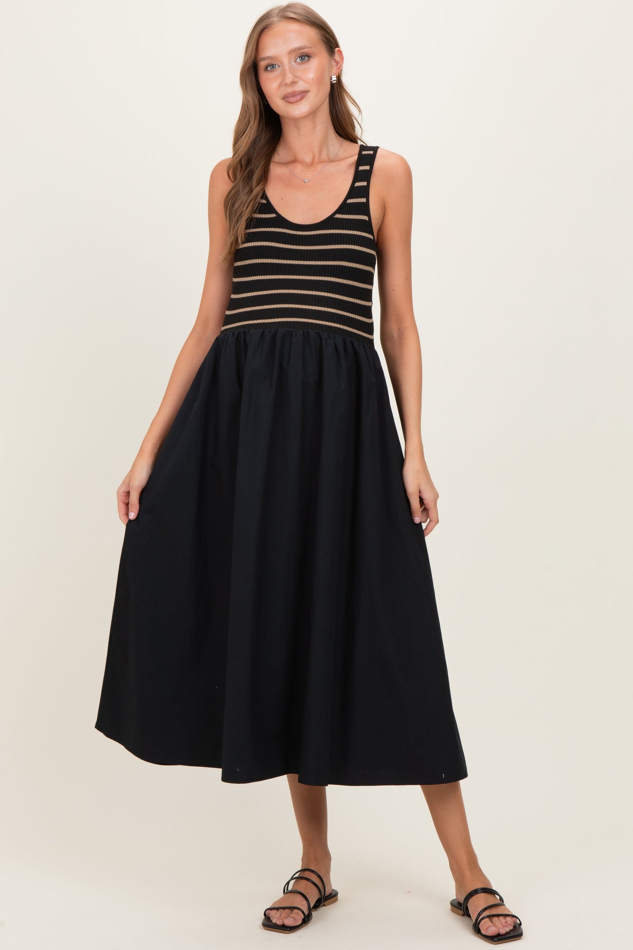 woman wearing a striped black and gold maternity dress with a flowing black skirt and sandals, showcasing her baby bump