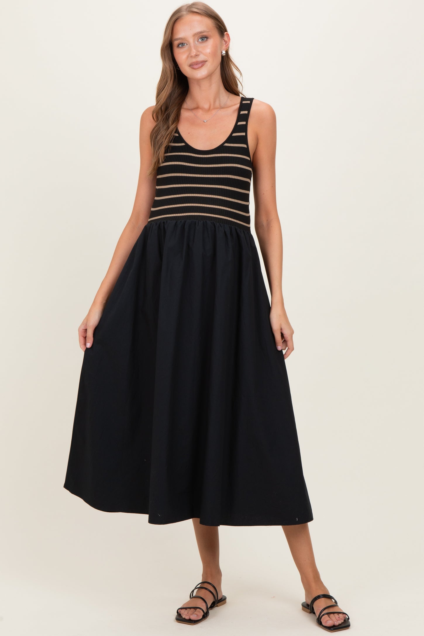 woman wearing a striped black and gold maternity dress with a flowing black skirt and sandals, showcasing her baby bump