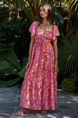 woman wearing a pink floral maxi dress with short ruffled sleeves standing outdoors among greenery