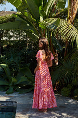 woman wearing a vibrant pink floral maxi dress with ruffled sleeves, standing in a tropical garden
