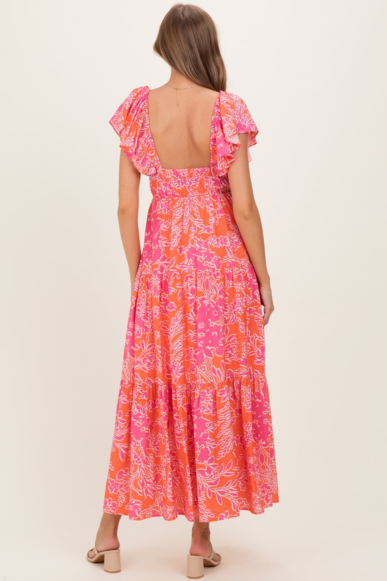 woman wearing a pink floral maxi maternity dress with ruffled sleeves, showing the back view