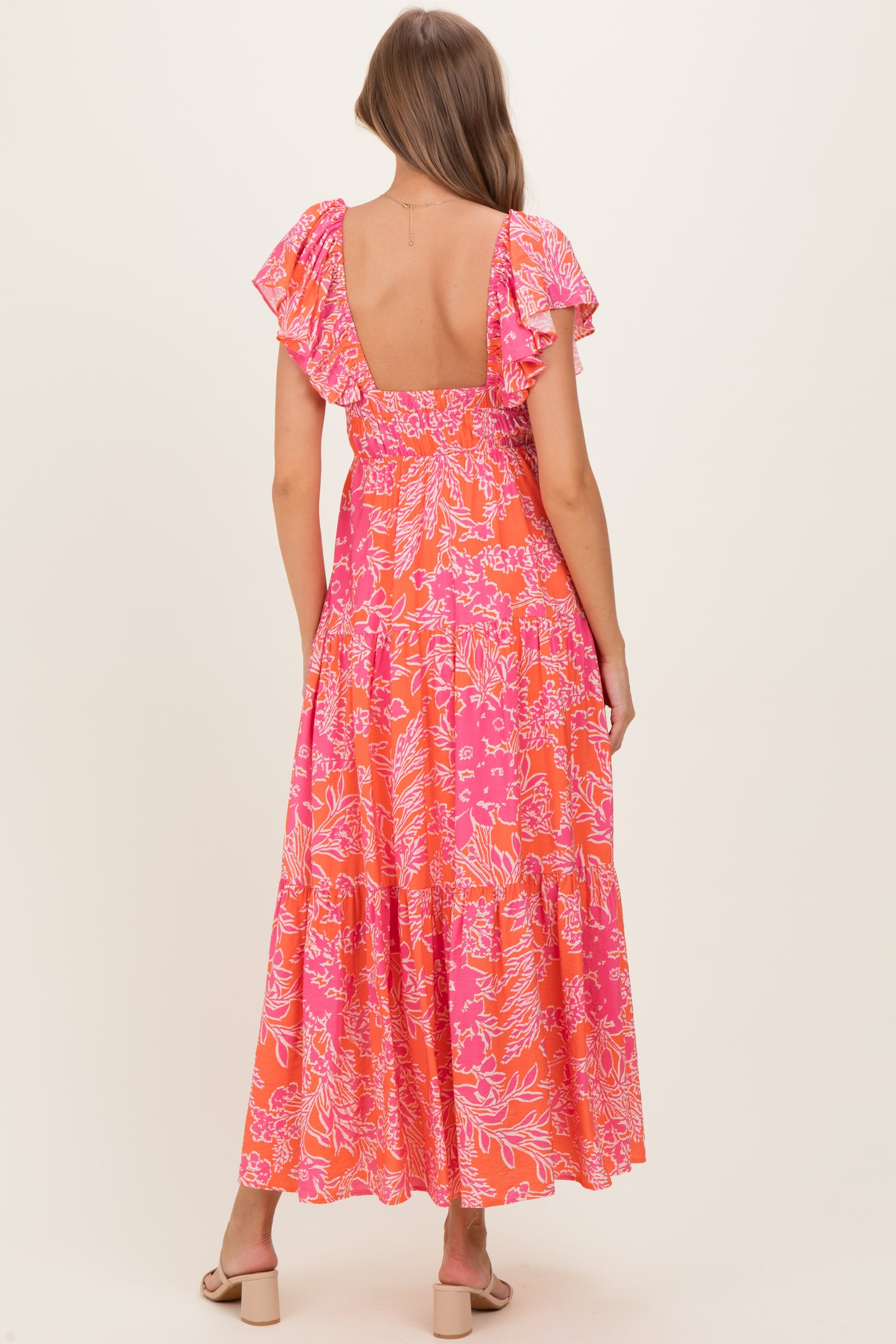 woman wearing a pink floral maxi maternity dress with ruffled sleeves, showing the back view