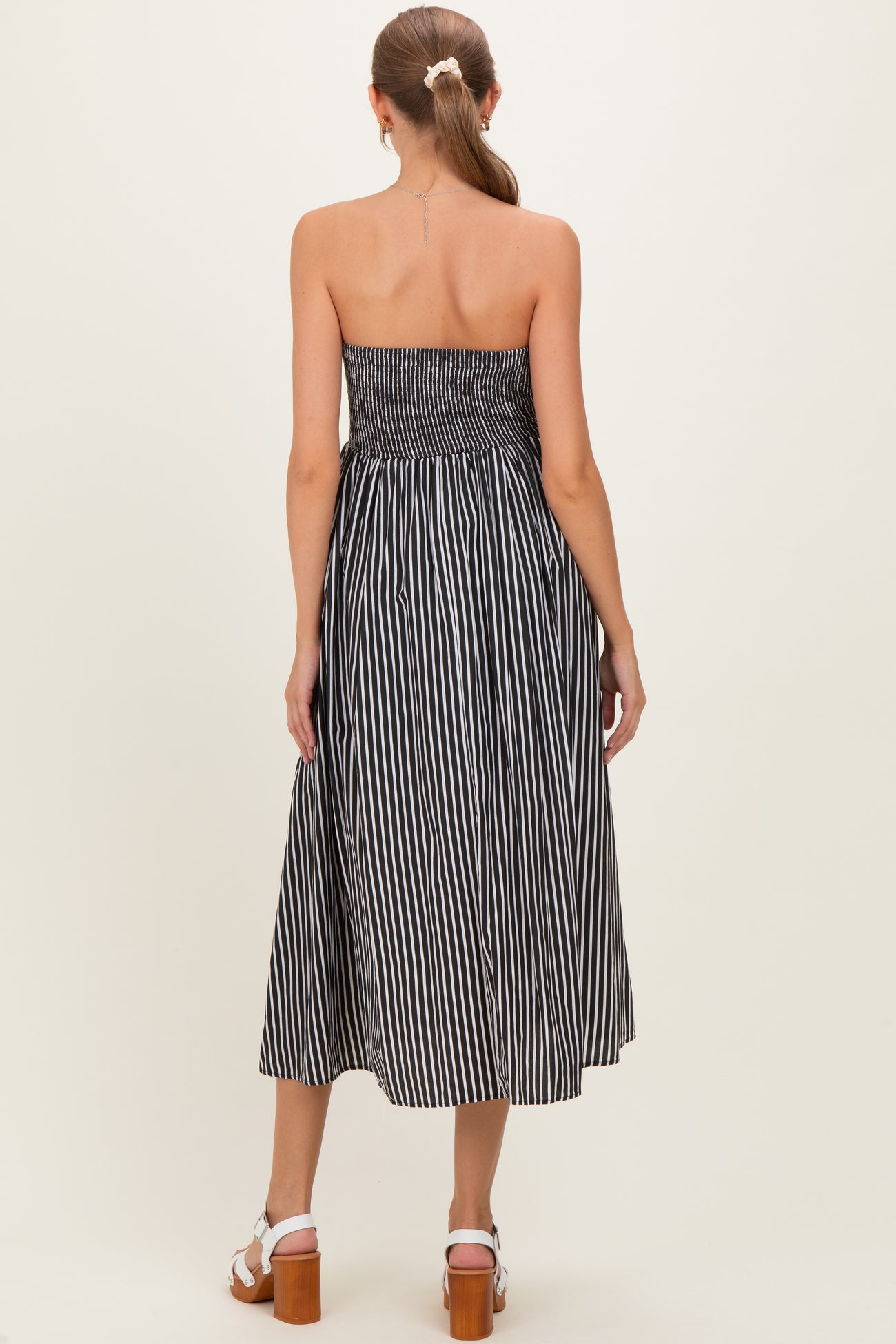 woman wearing a black and white striped strapless maternity dress with a smocked bodice and flowing skirt