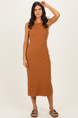 woman wearing a tan sleeveless maxi dress with a fitted silhouette and standing with one hand in her hair