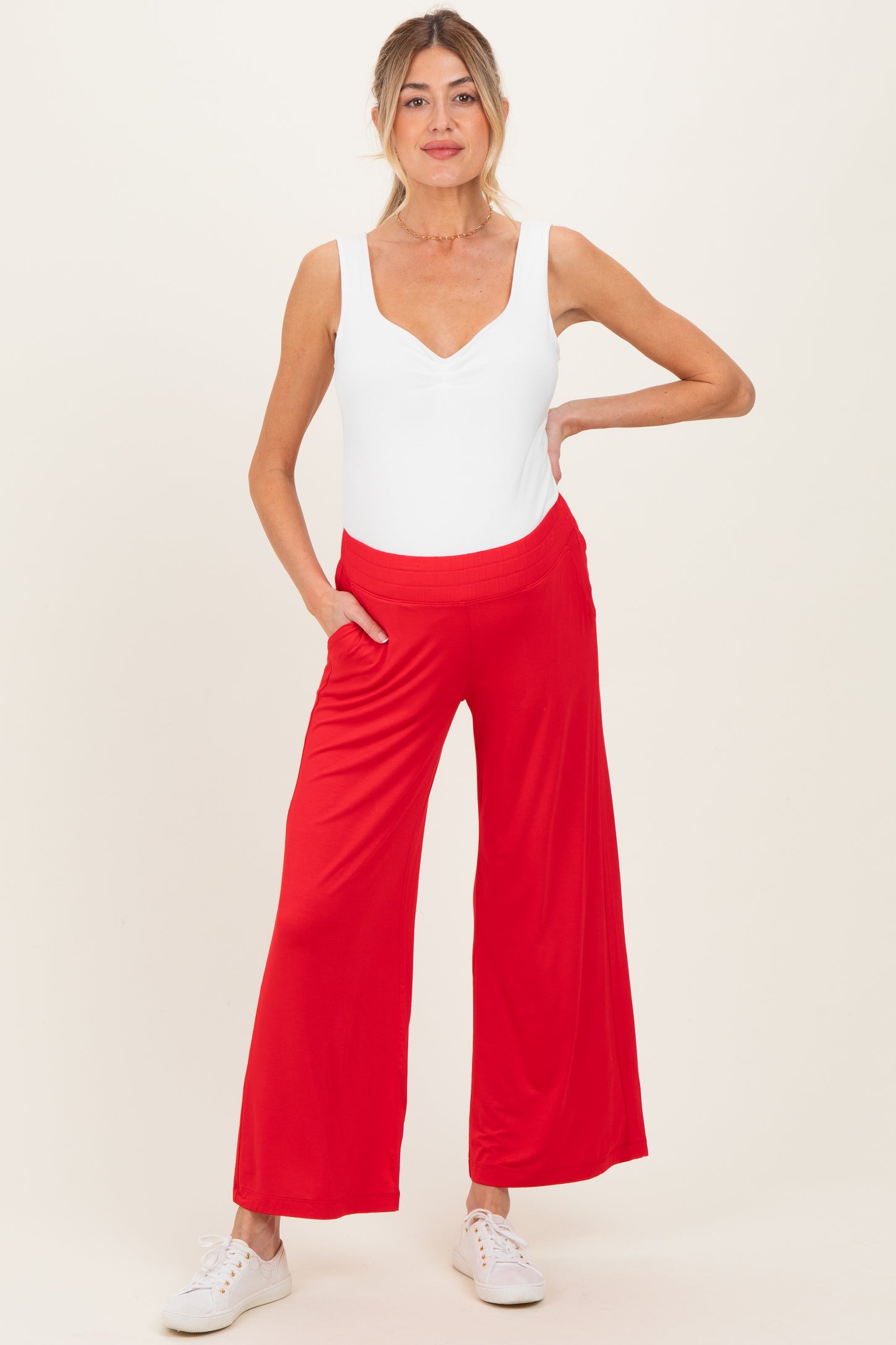 woman wearing a white nursing bodysuit and red wide-leg maternity pants with pockets