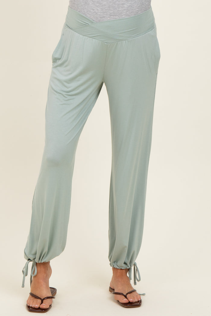 woman wearing light green maternity pants with a wide waistband and adjustable ties at the ankles