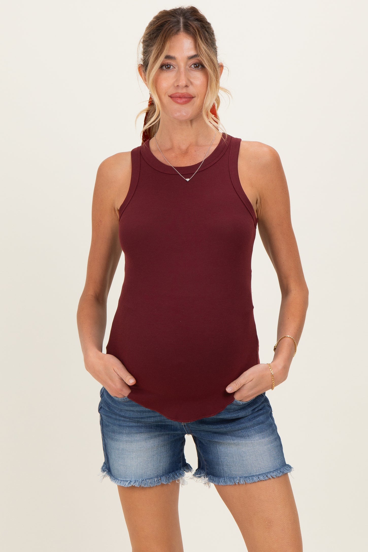 woman wearing a burgundy maternity tank top and denim shorts, highlighting her baby bump