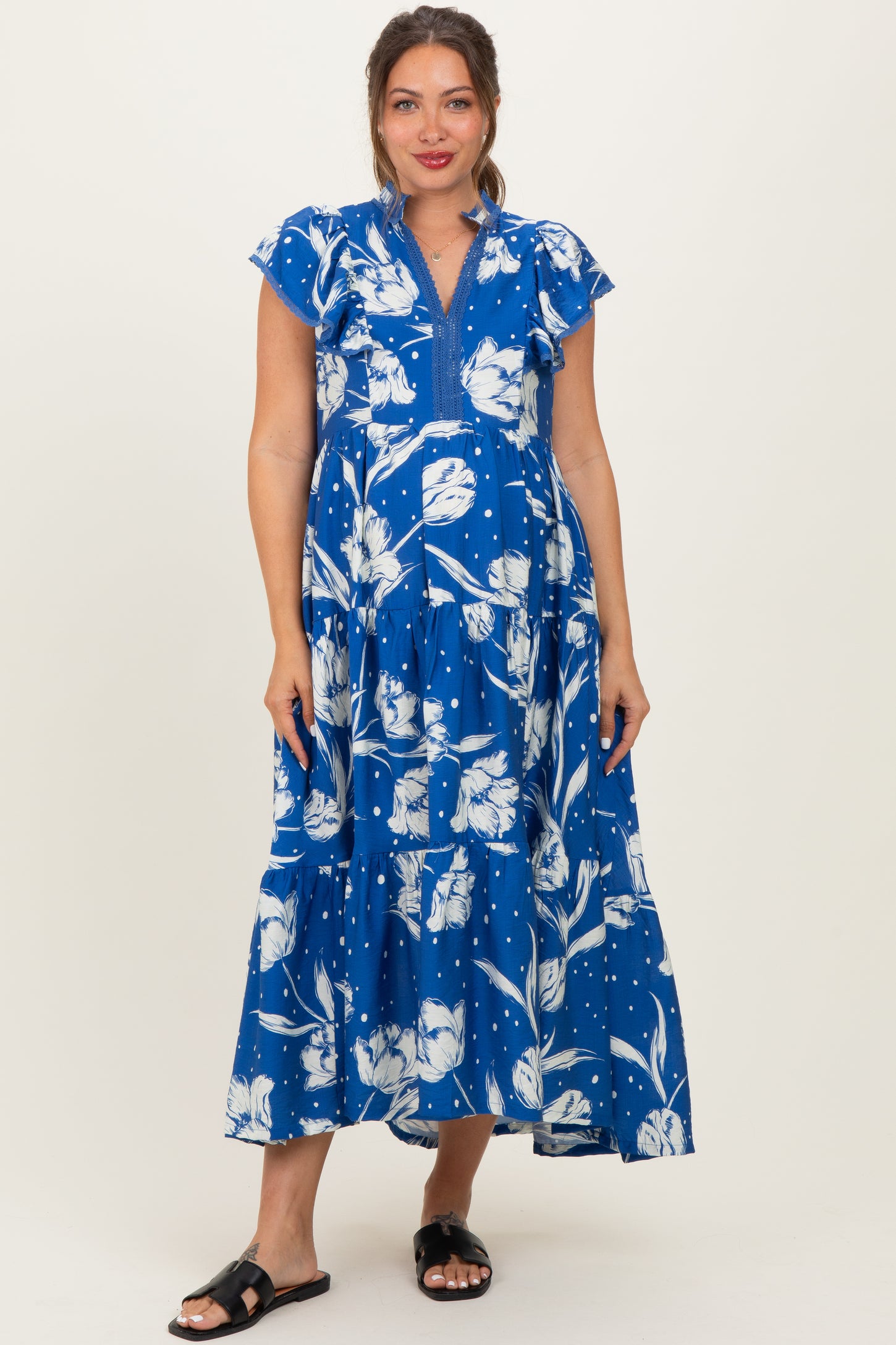 woman wearing a blue floral maternity dress with cap sleeves and tiered skirt, showcasing her baby bump