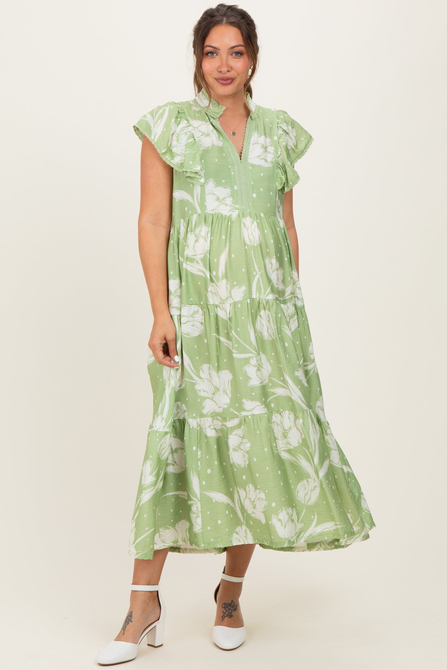 woman wearing a green floral maternity maxi dress with flutter sleeves and tiered design, showcasing her baby bump