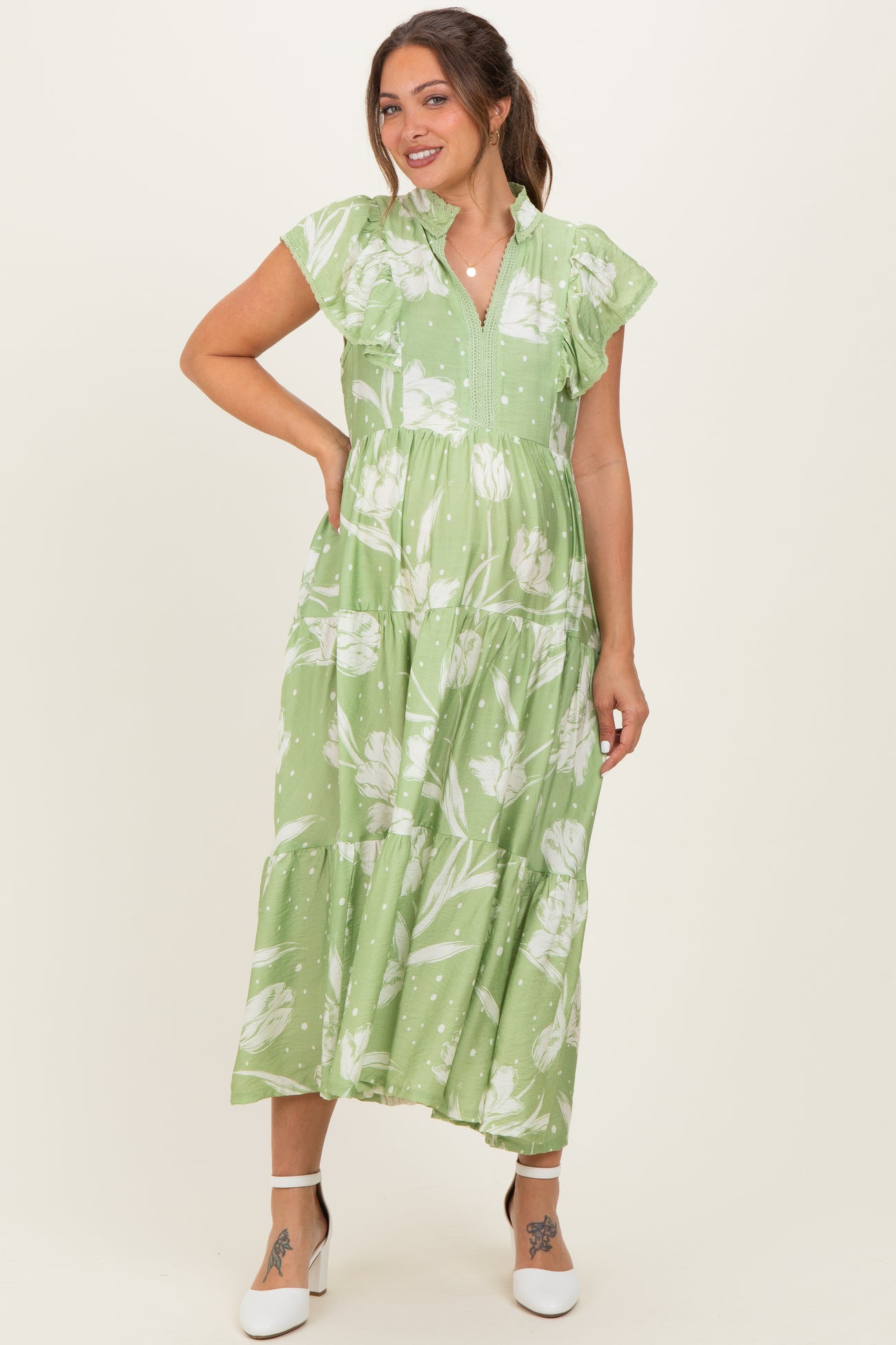 woman wearing a green floral maternity dress with short ruffled sleeves and a tiered skirt, showcasing her baby bump