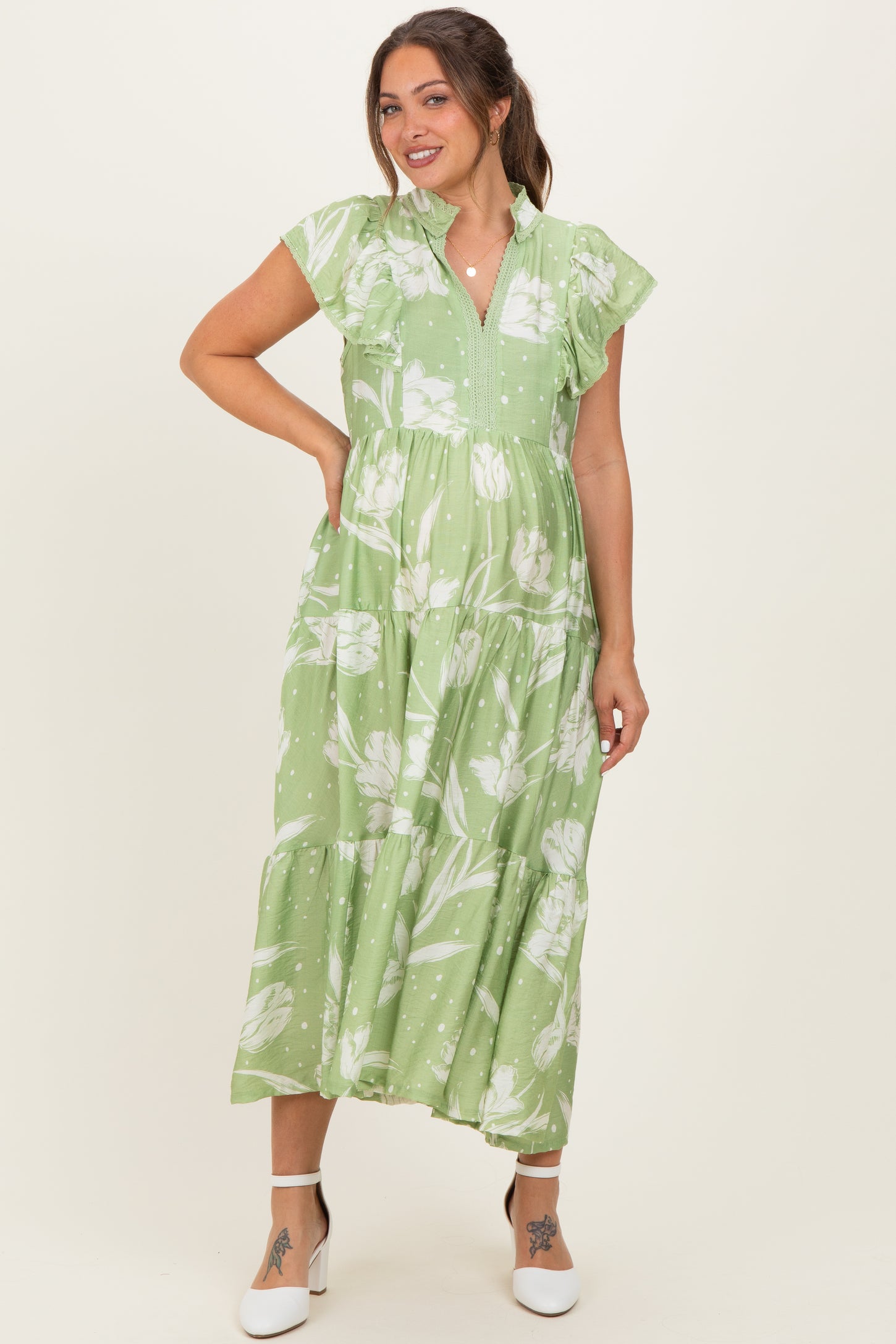 woman wearing a green floral maternity dress with short ruffled sleeves and a tiered skirt, showcasing her baby bump