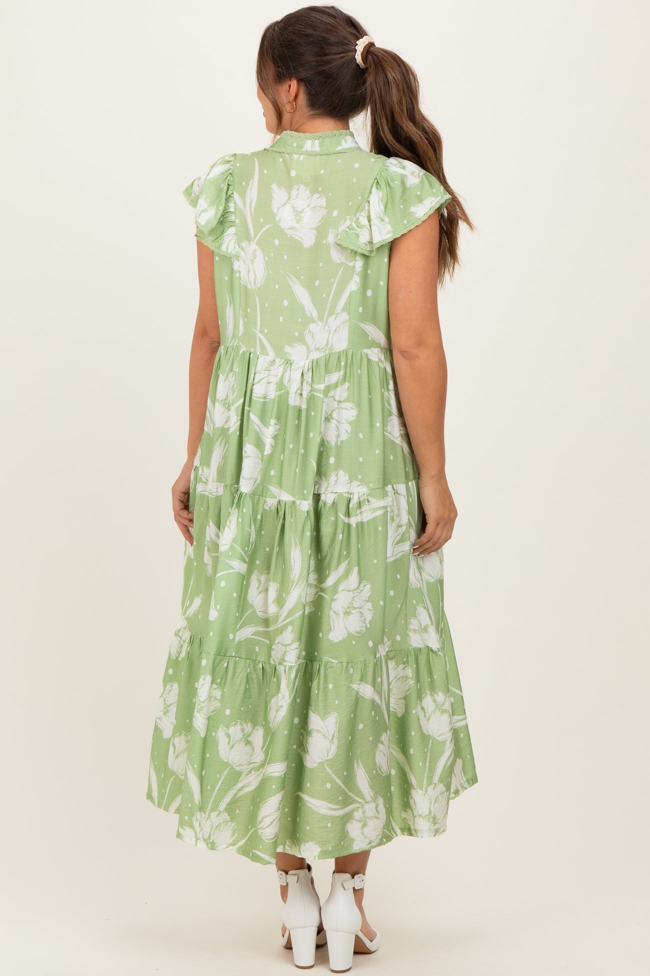 woman wearing a green floral maternity maxi dress with ruffled sleeves and a tiered design, showing her back