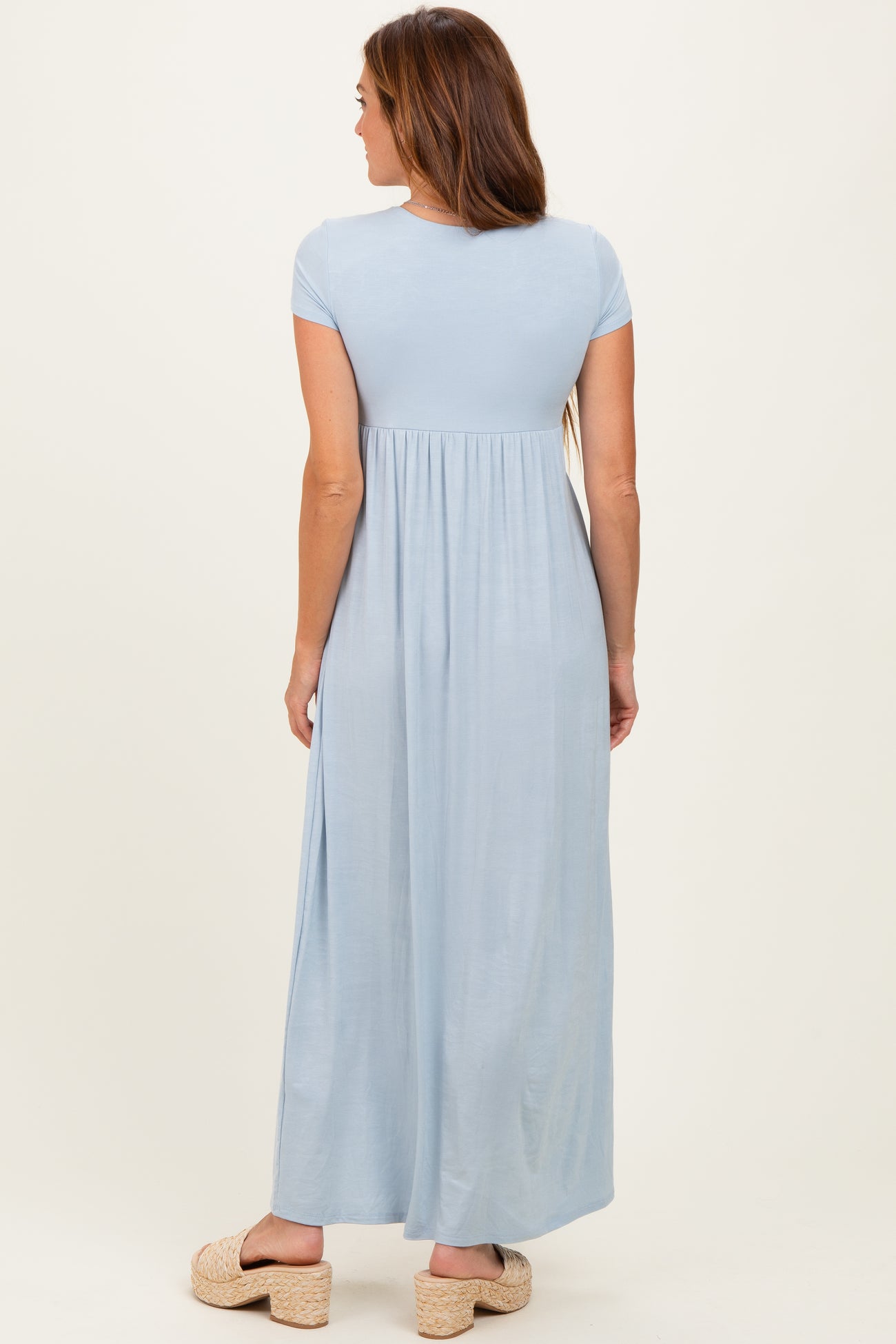 woman wearing a light blue maxi dress with a fitted top and flowy skirt, standing with her back to the camera