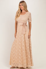 woman wearing a blush lace maxi dress with short sleeves and a ribbon belt tied at the waist