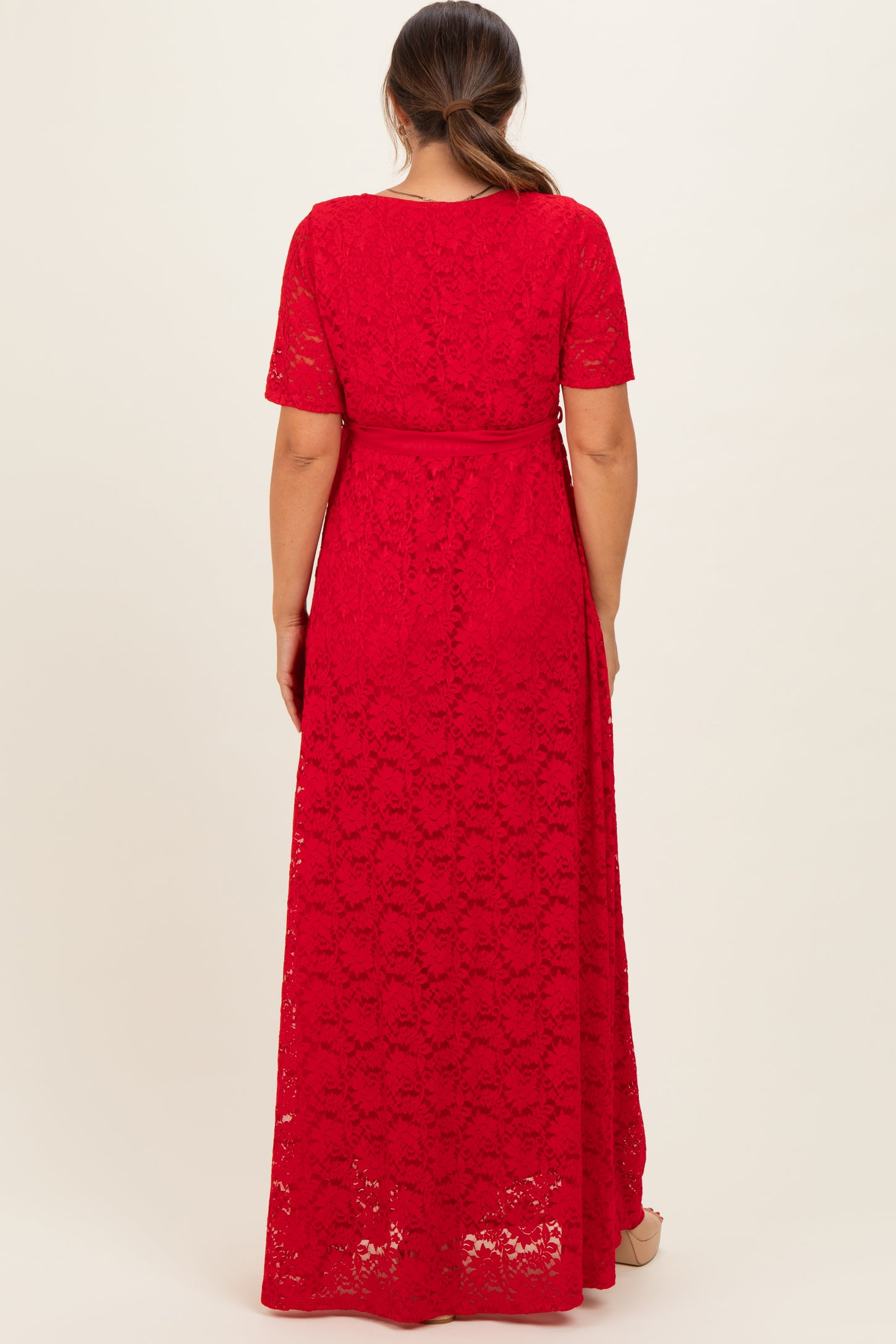 woman wearing a red lace maternity maxi dress with short sleeves and a tie waist detail, showing a baby bump