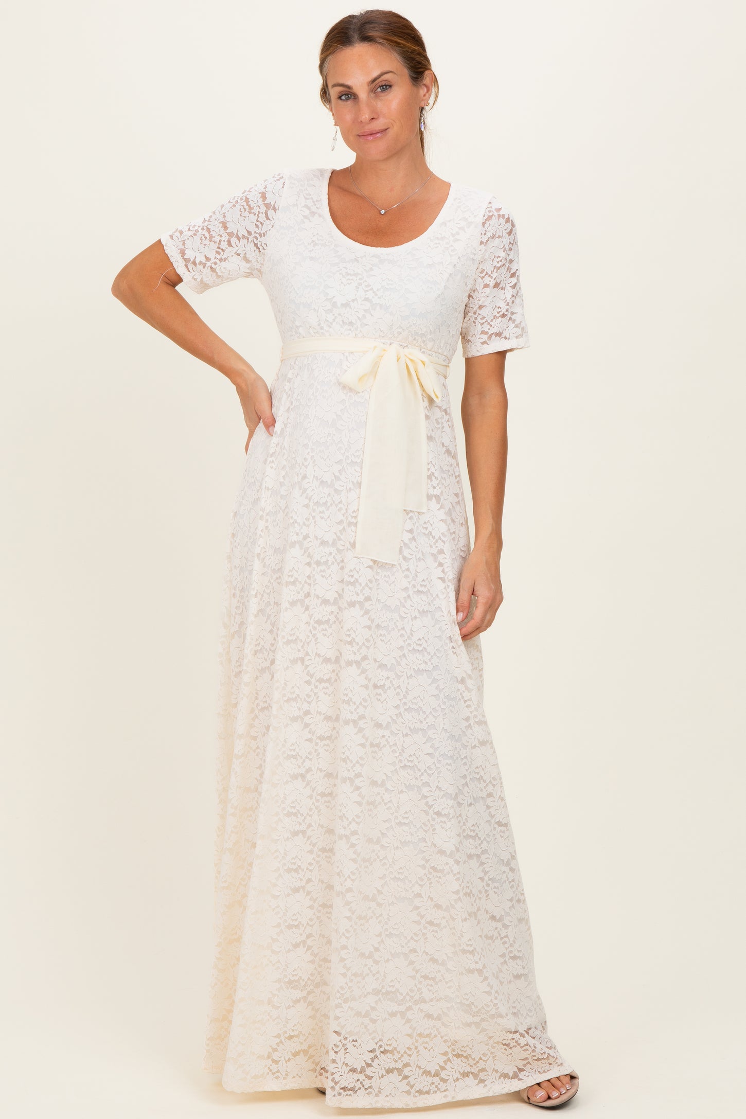 woman wearing a cream lace maxi dress with a short sleeve and a satin waist tie