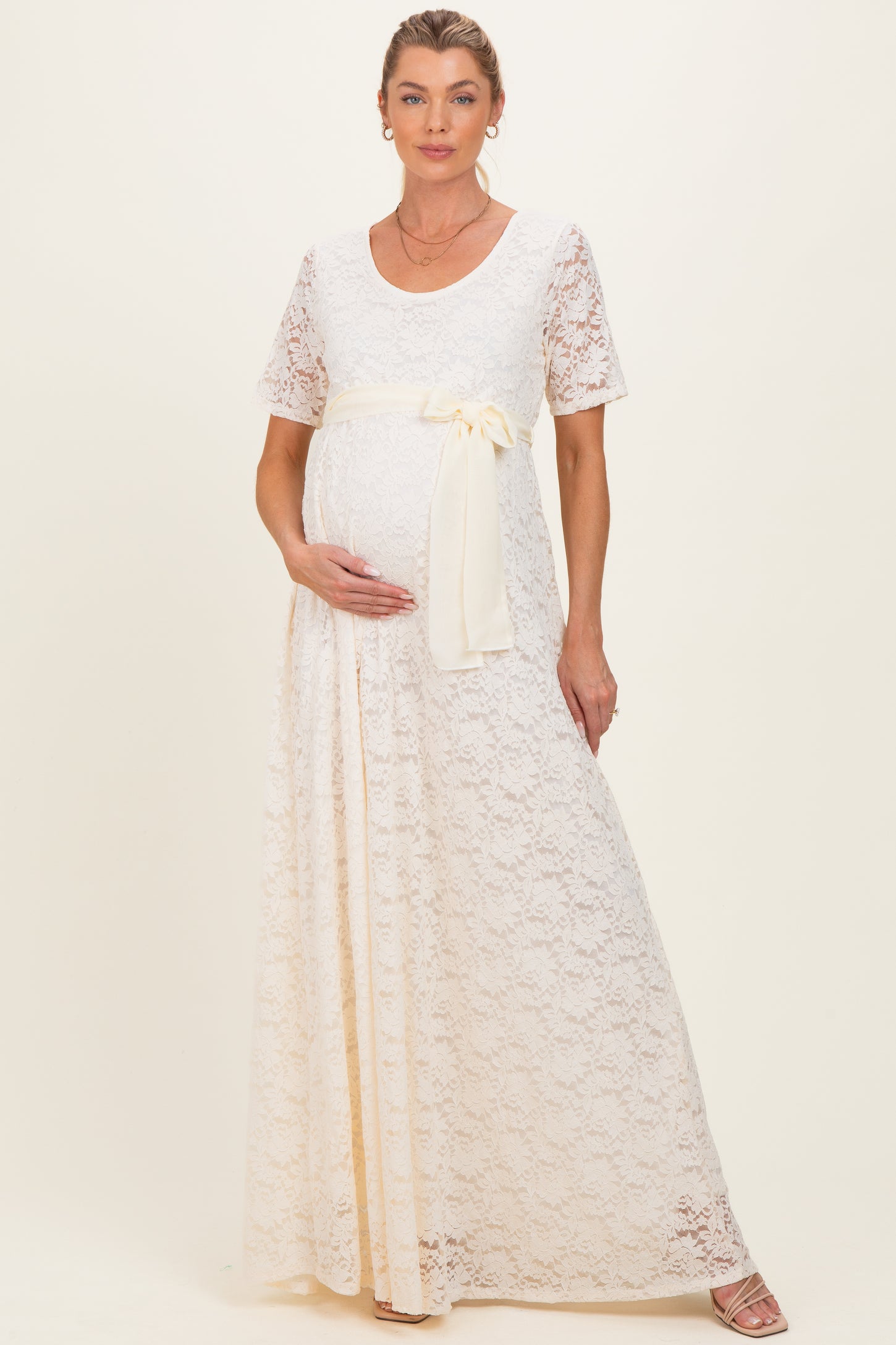woman wearing a cream lace maternity gown with short sleeves and a tie waist, showing her baby bump