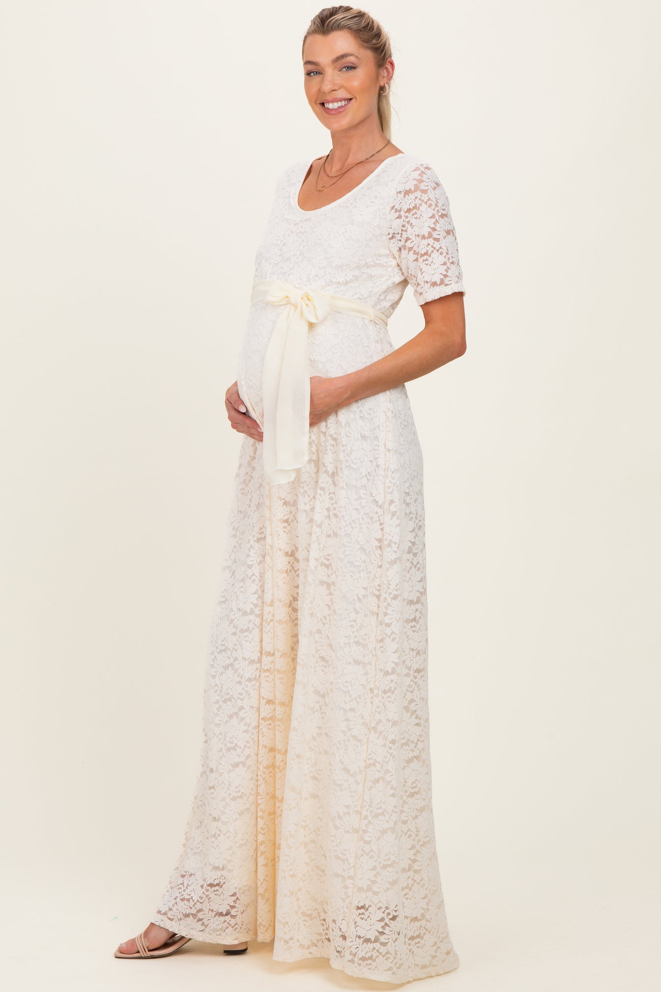 woman wearing a cream lace maternity dress with a bow detail, showcasing her baby bump