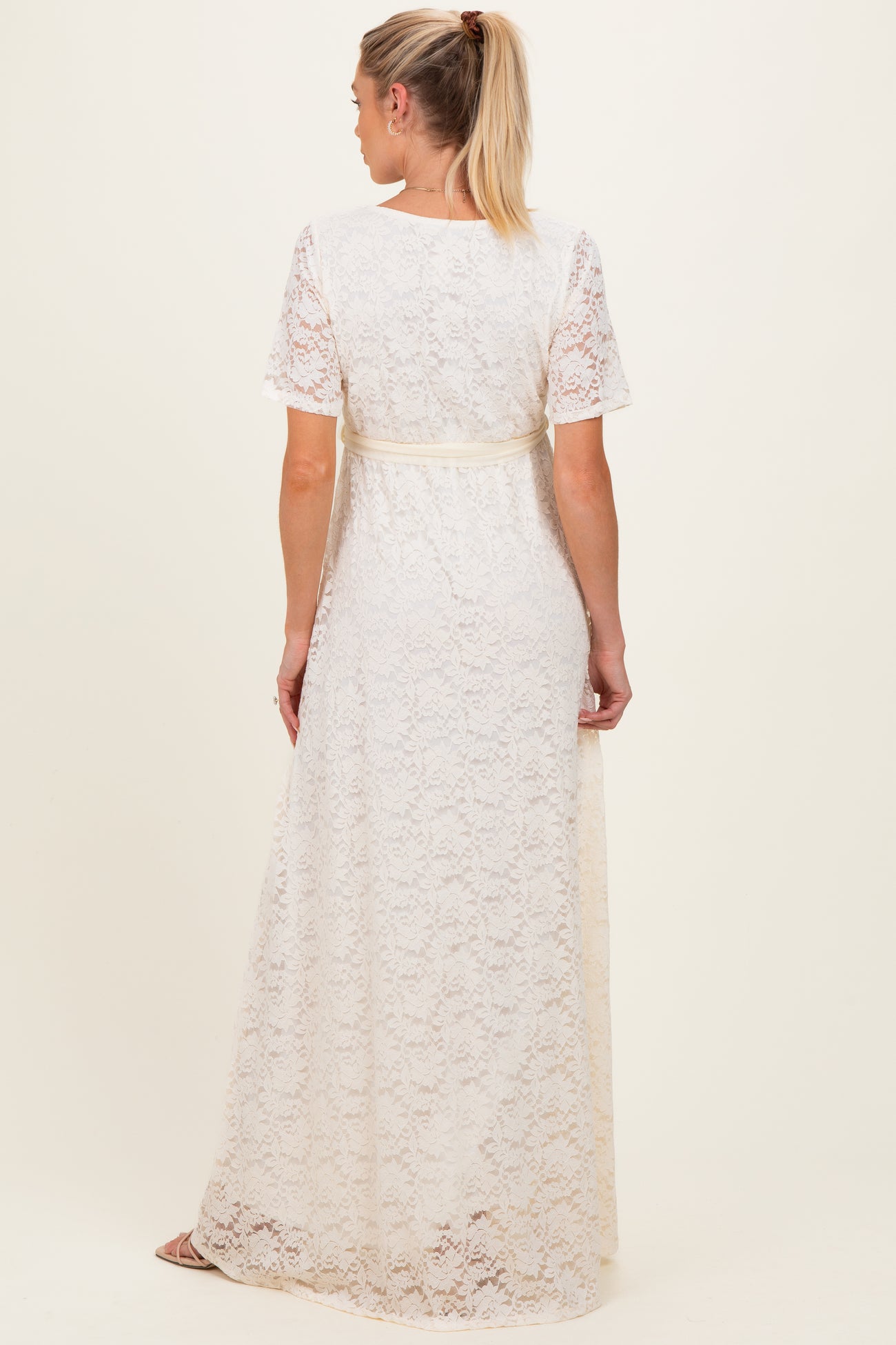 woman wearing a white lace maternity maxi dress with short sleeves and a tied waist, showing the back view