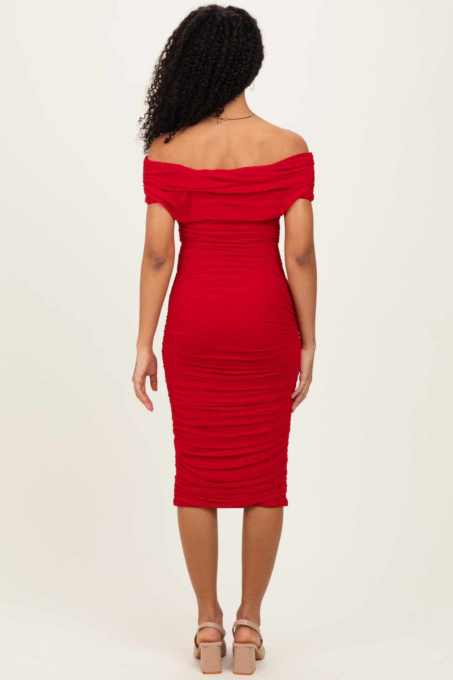 woman wearing a red off-the-shoulder fitted midi dress with ruching details, viewed from the back