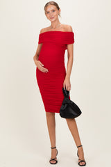 woman wearing a red off-the-shoulder ruched maternity dress and holding her baby bump