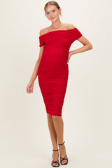 woman wearing a red off-shoulder ruched maternity dress, showcasing her baby bump and styled with black heels
