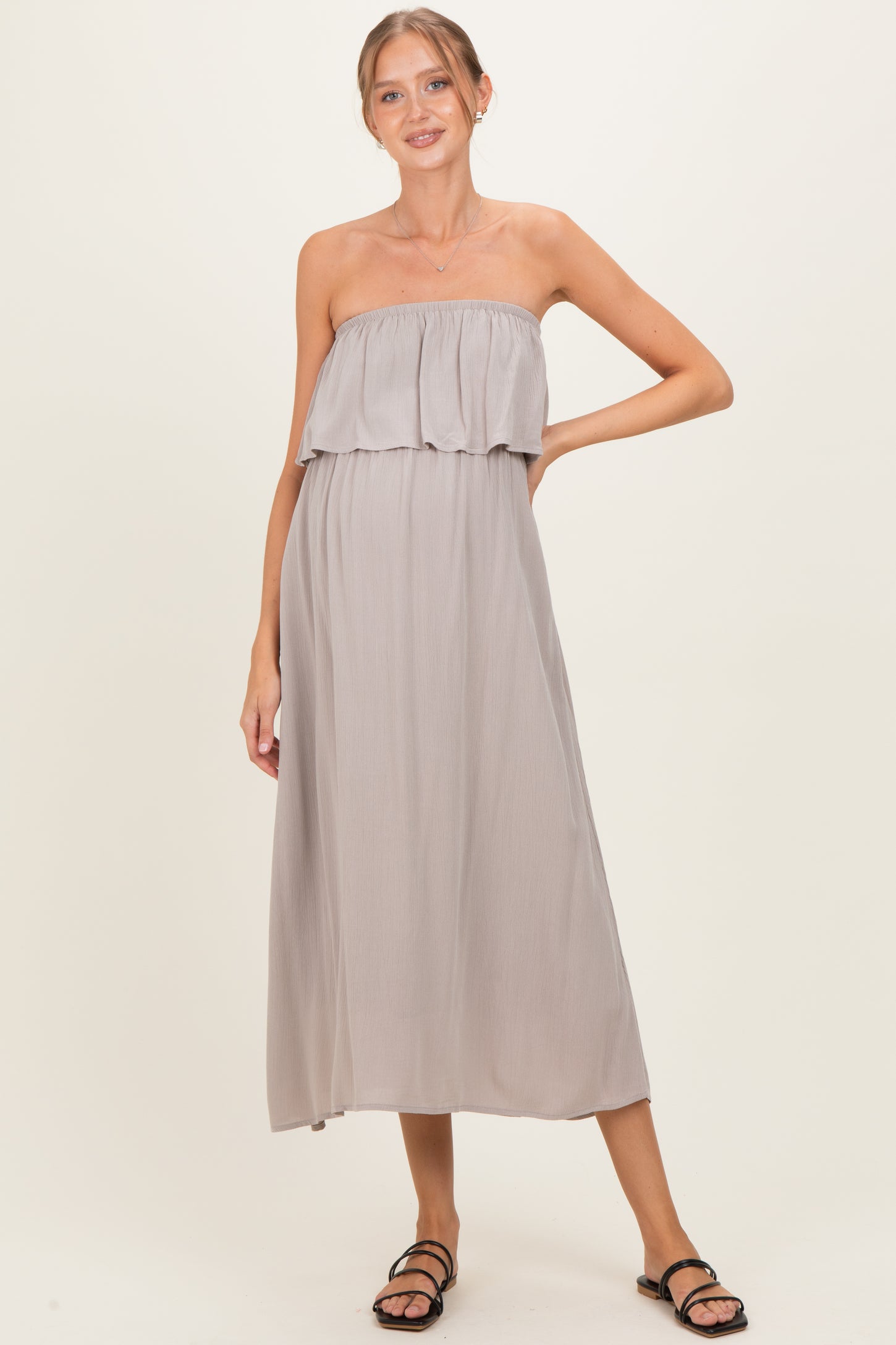 woman wearing a light grey strapless maternity dress with a ruffled overlay and a flowing silhouette