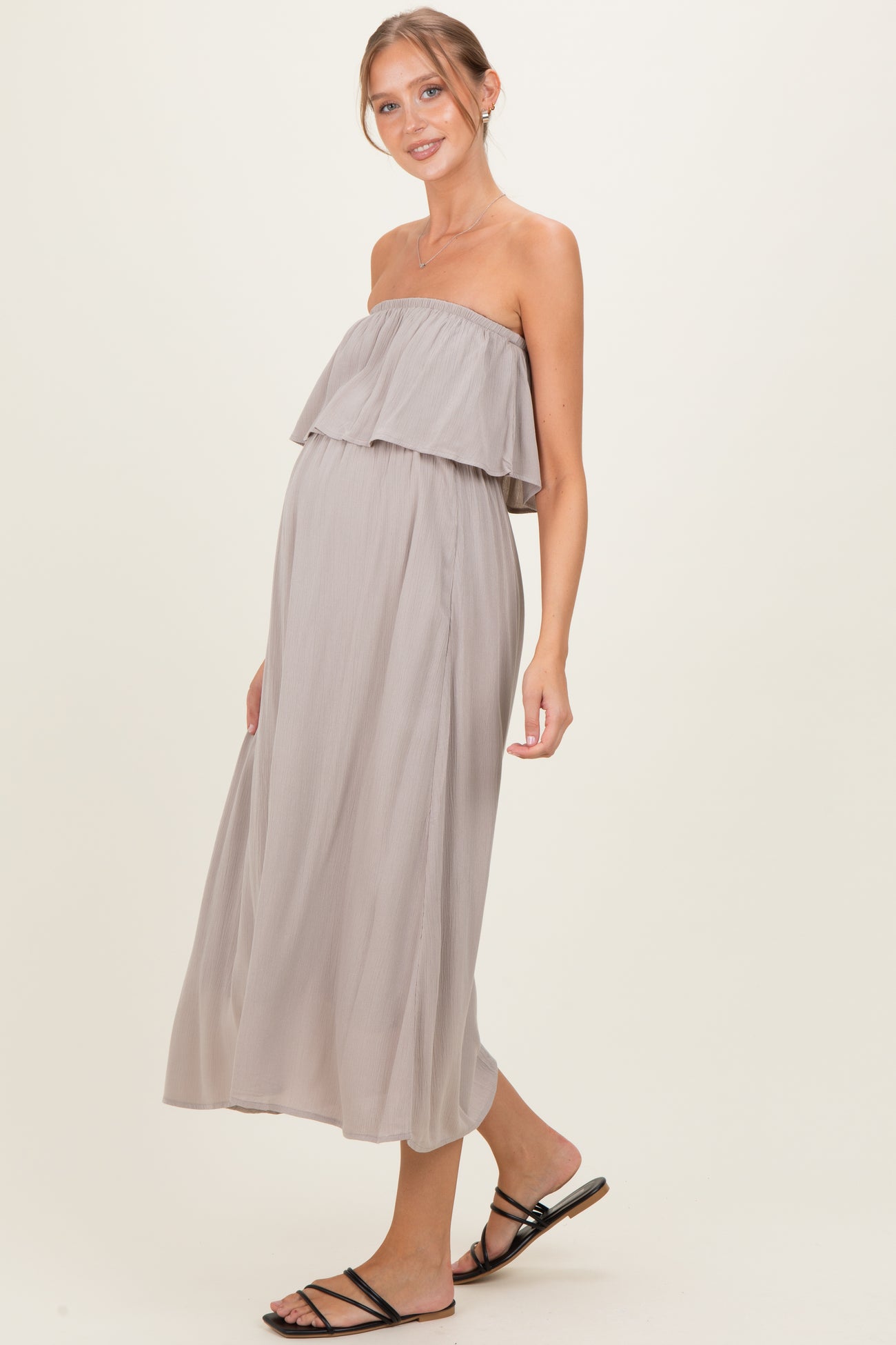 woman wearing a strapless taupe maternity maxi dress with ruffled details and a visible baby bump