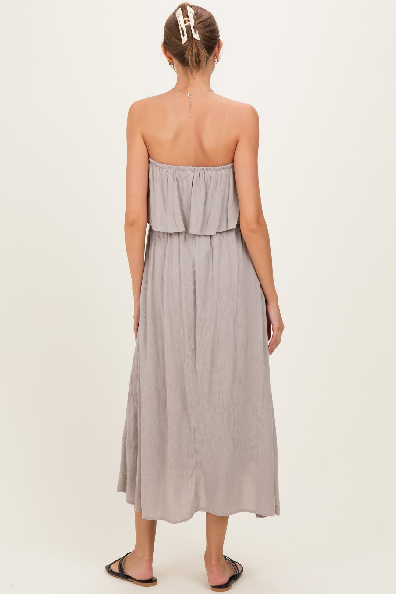 woman wearing a gray strapless maternity maxi dress with a layered ruffle detail, showing her back