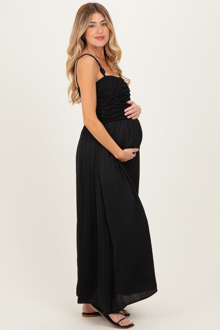 woman wearing a black maternity maxi dress with ruffle detailing and holding her baby bump