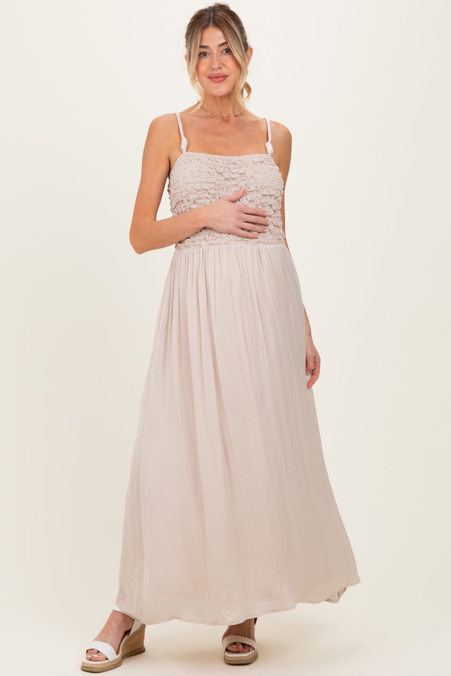 woman wearing a light beige maternity maxi dress with a smocked bodice, holding her baby bump