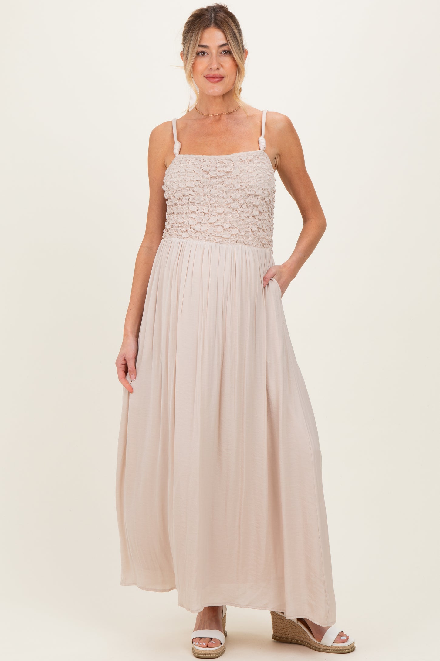 woman wearing a light beige maternity maxi dress with a textured bodice and pockets