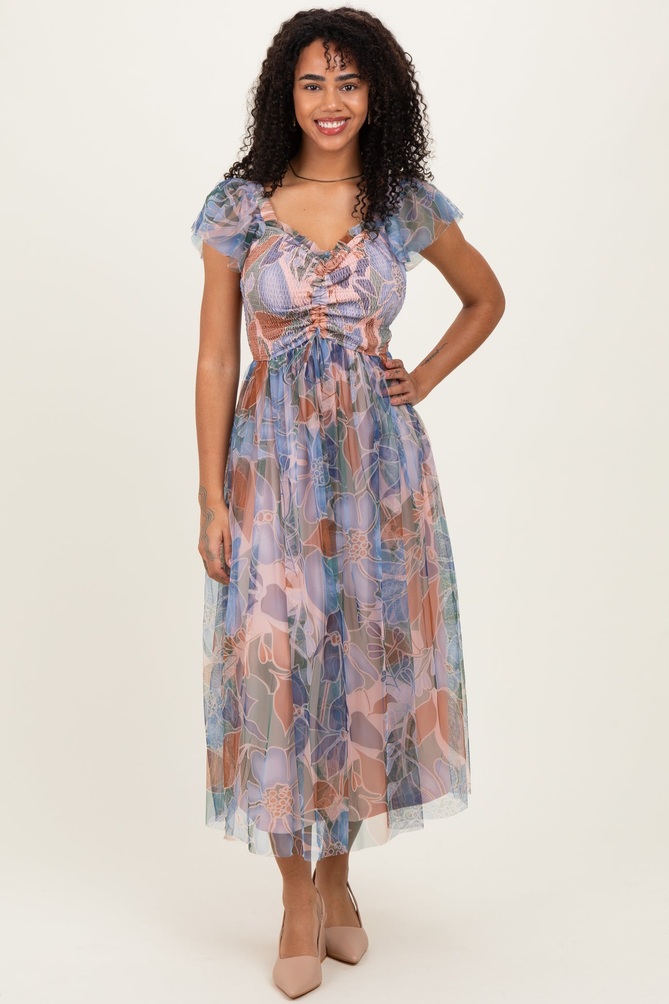 woman wearing a floral sheer maxi dress with puff sleeves and a cinched waist in pastel colors.