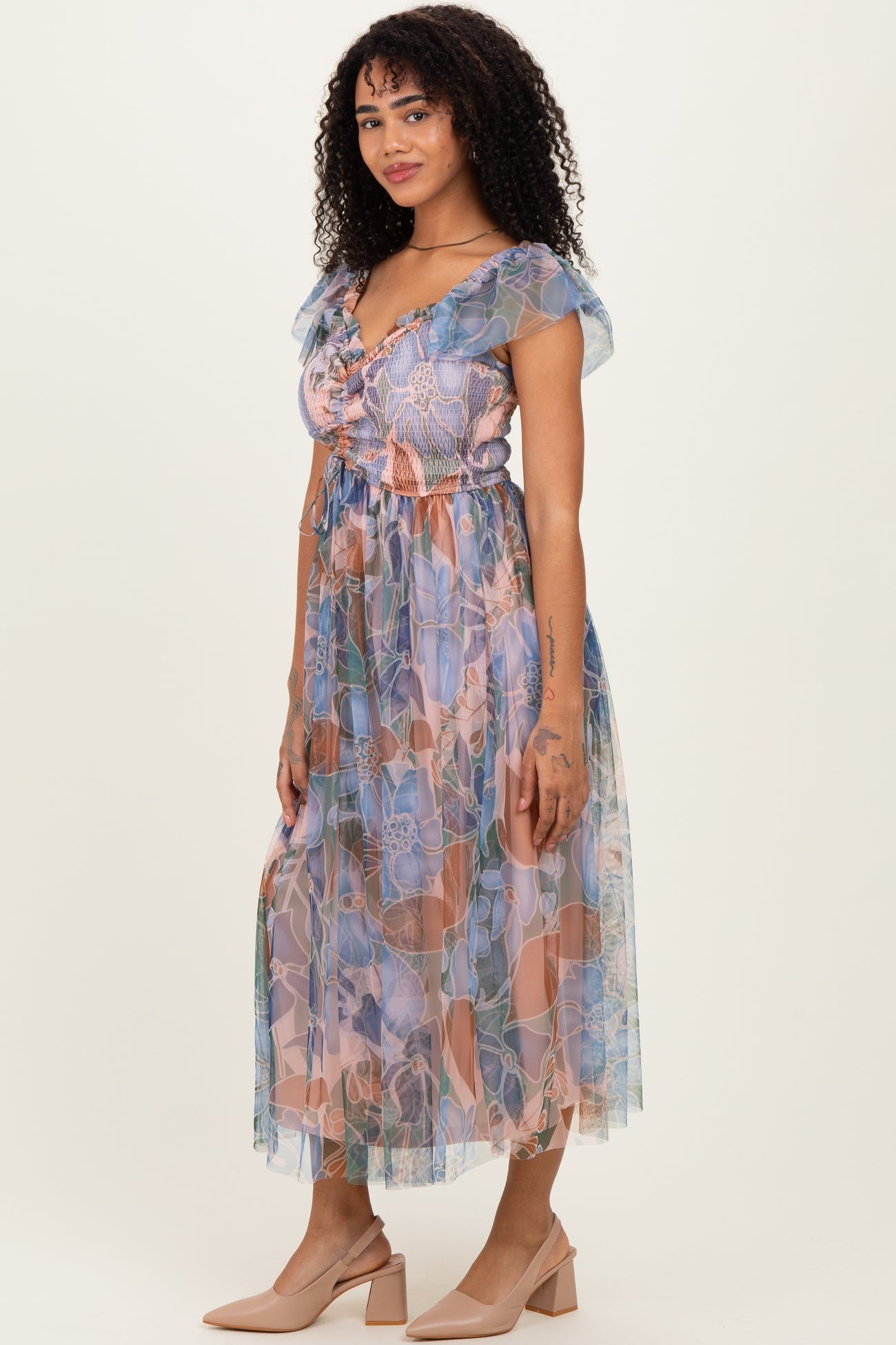 woman wearing a patterned pastel maxi dress with short ruffled sleeves and a cinched waist, styled with nude heels