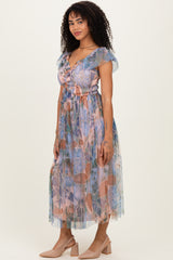 woman wearing a patterned pastel maxi dress with short ruffled sleeves and a cinched waist, styled with nude heels