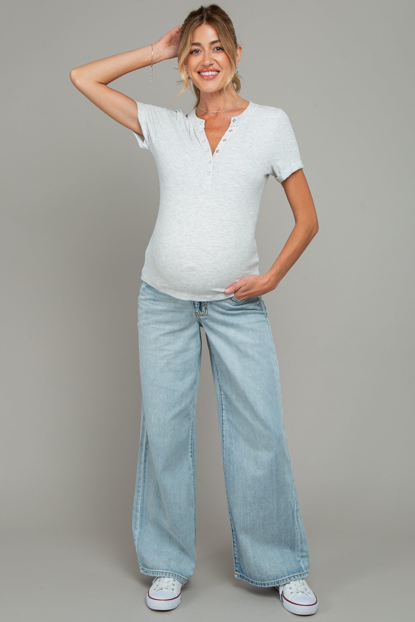 woman wearing a light gray maternity henley top and wide-leg jeans, showing her baby bump