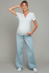 woman wearing a light gray maternity henley top and wide-leg jeans, showing her baby bump