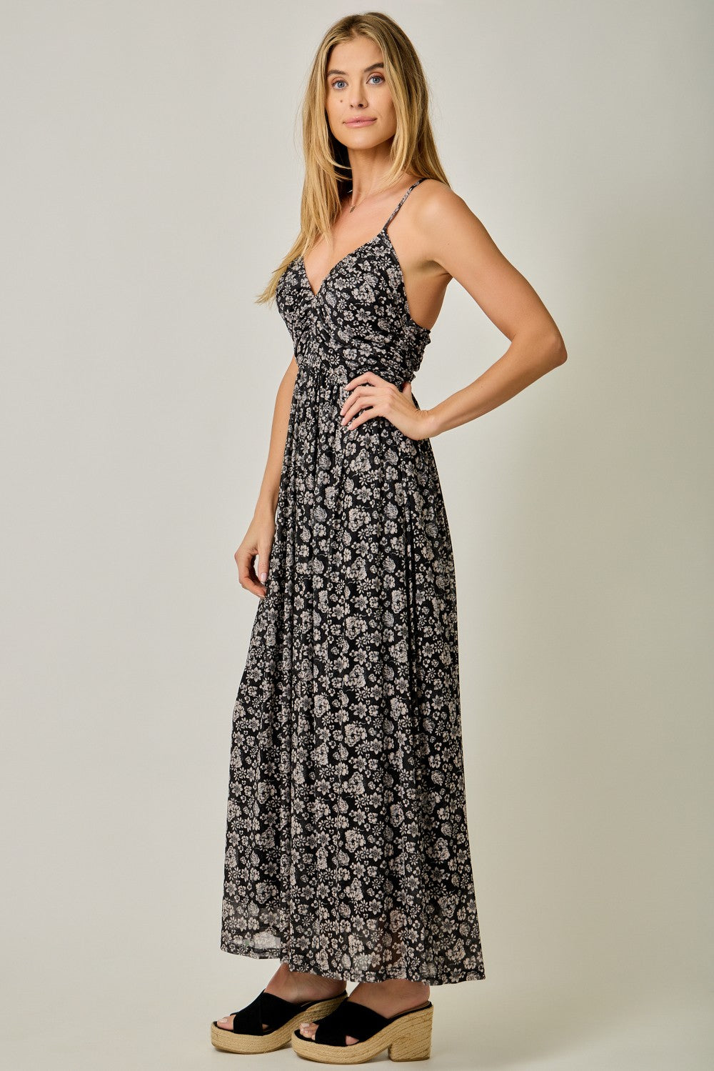 woman wearing a black floral maxi dress with thin straps and a flowy silhouette, standing in profile
