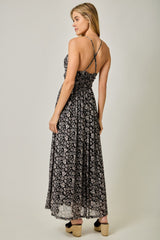 woman wearing a black floral maxi dress with thin straps and a flowy skirt, standing with her back to the camera
