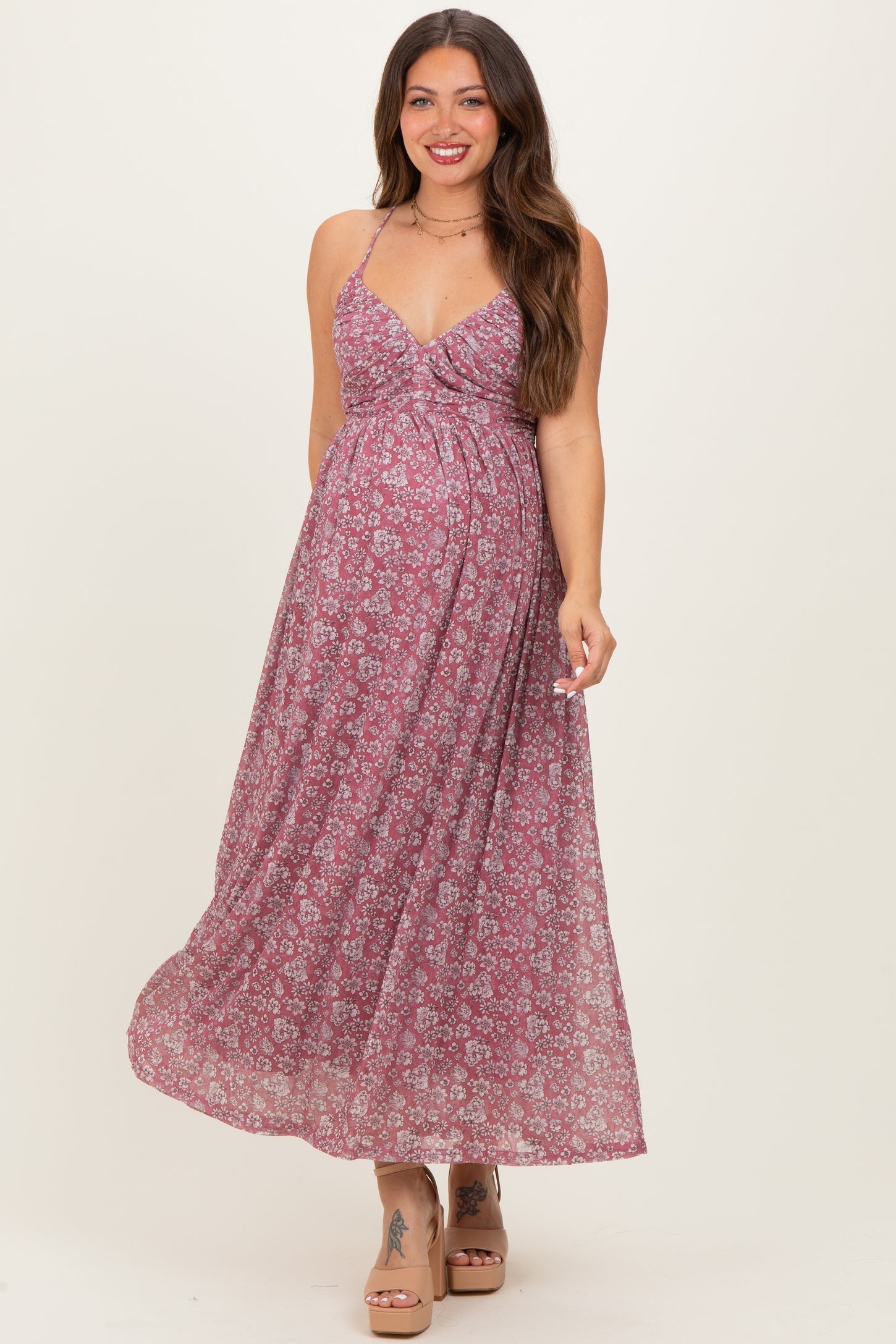 woman wearing a floral pink maternity maxi dress with a fitted bodice and flowing skirt, showing her baby bump