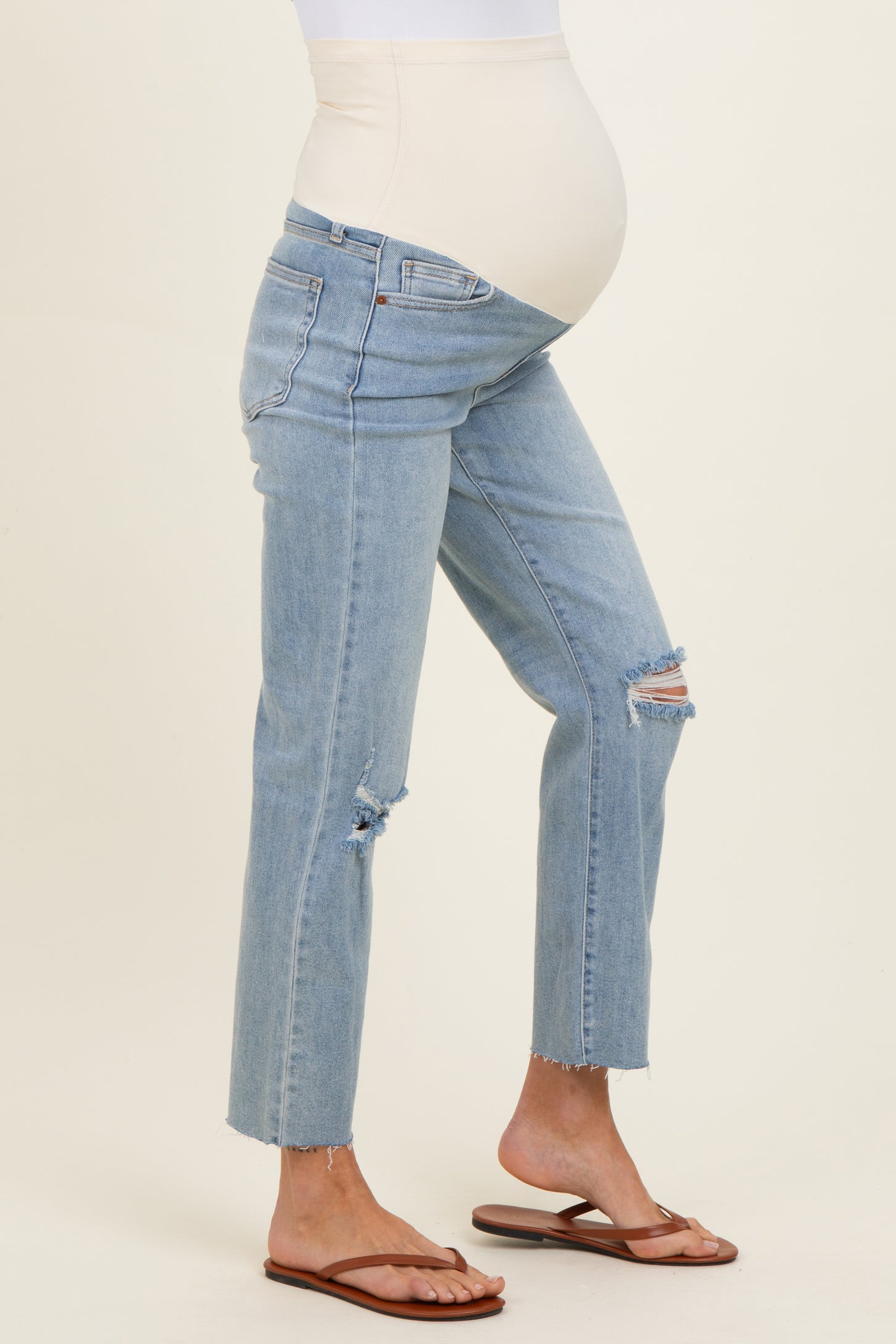 woman wearing light blue maternity jeans with a distressed style and a supportive over-the-bump waistband, showing a baby bump
