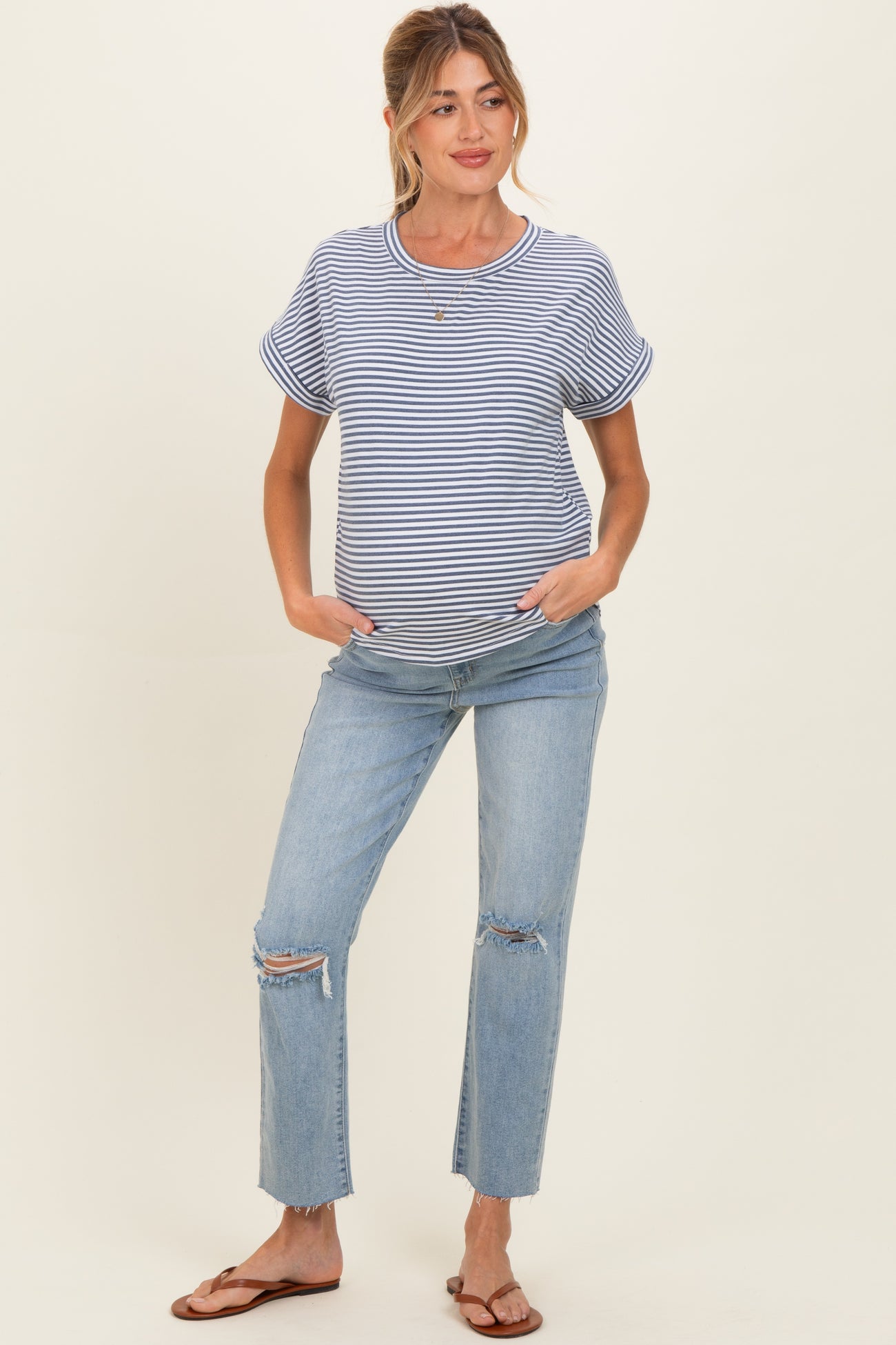 woman wearing a navy and white striped maternity t-shirt and distressed light blue jeans with a visible baby bump