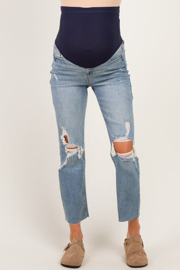 woman wearing distressed light wash maternity jeans with a navy blue over-the-bump waistband and exposed knees