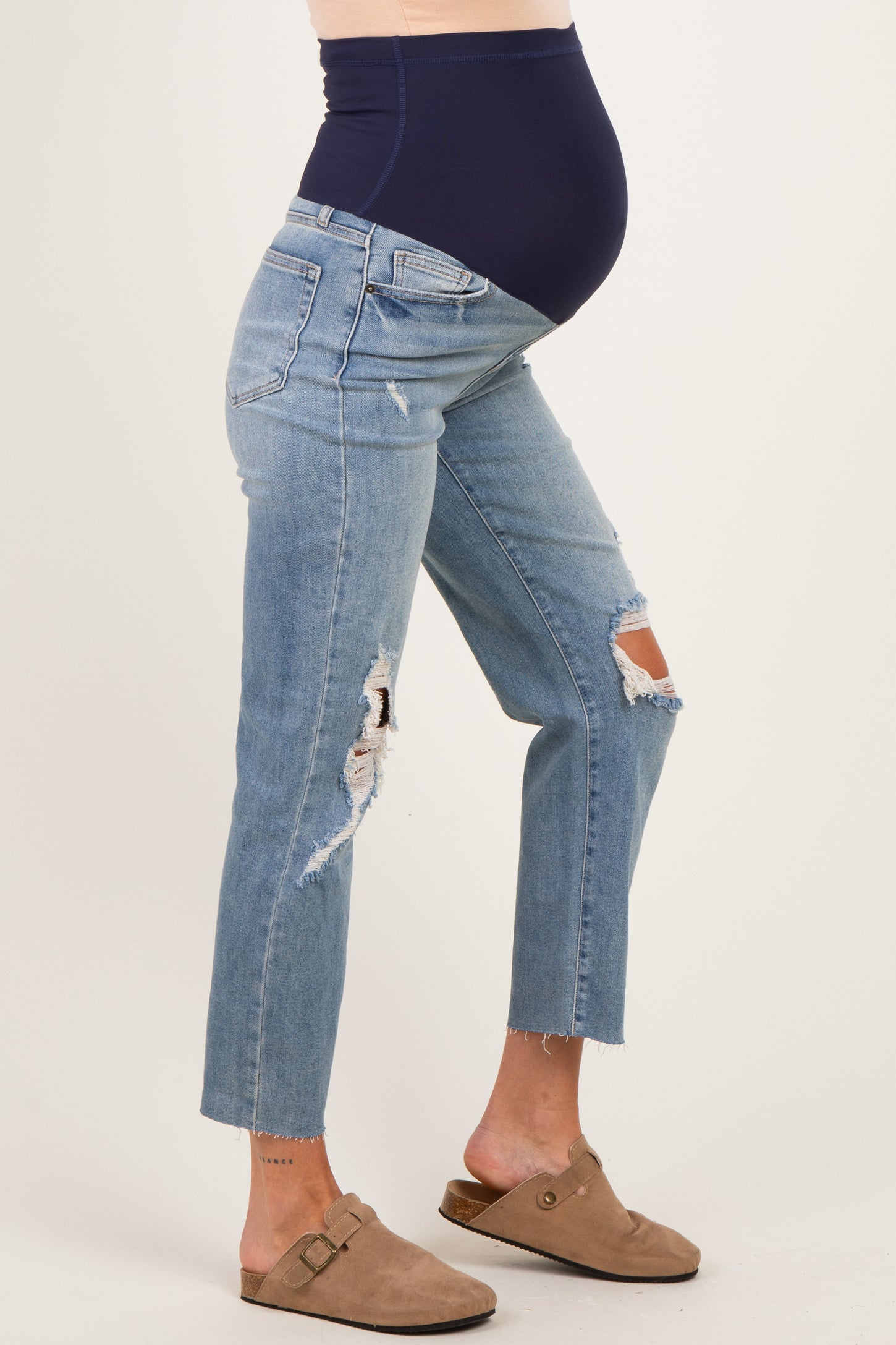 woman wearing distressed light blue maternity jeans with a navy blue over-the-belly panel and a visible baby bump