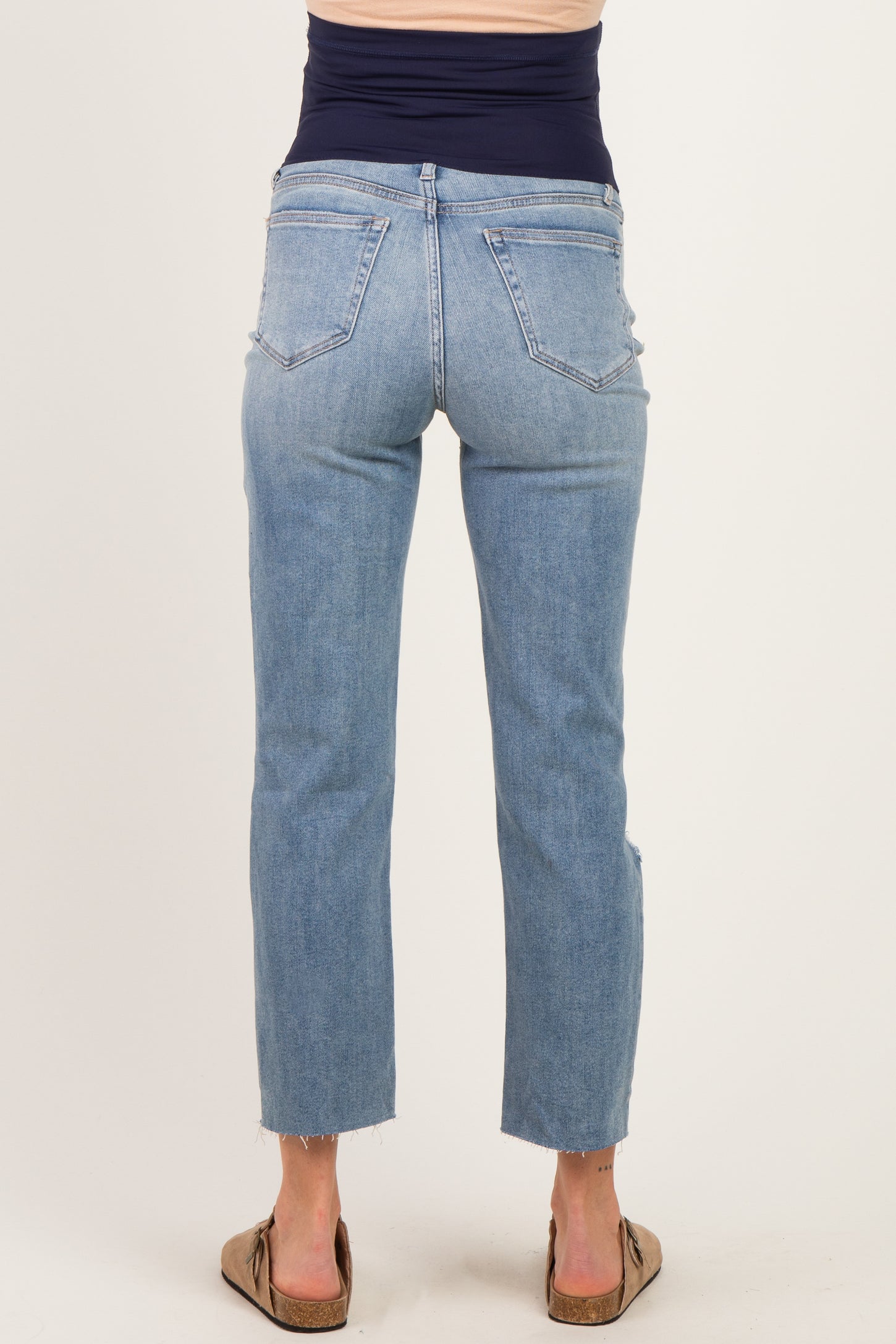 woman wearing light blue maternity jeans with a frayed hem, showing a fitted waistband and back view