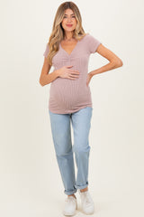 woman wearing a light pink ribbed maternity top and blue jeans, holding her baby bump