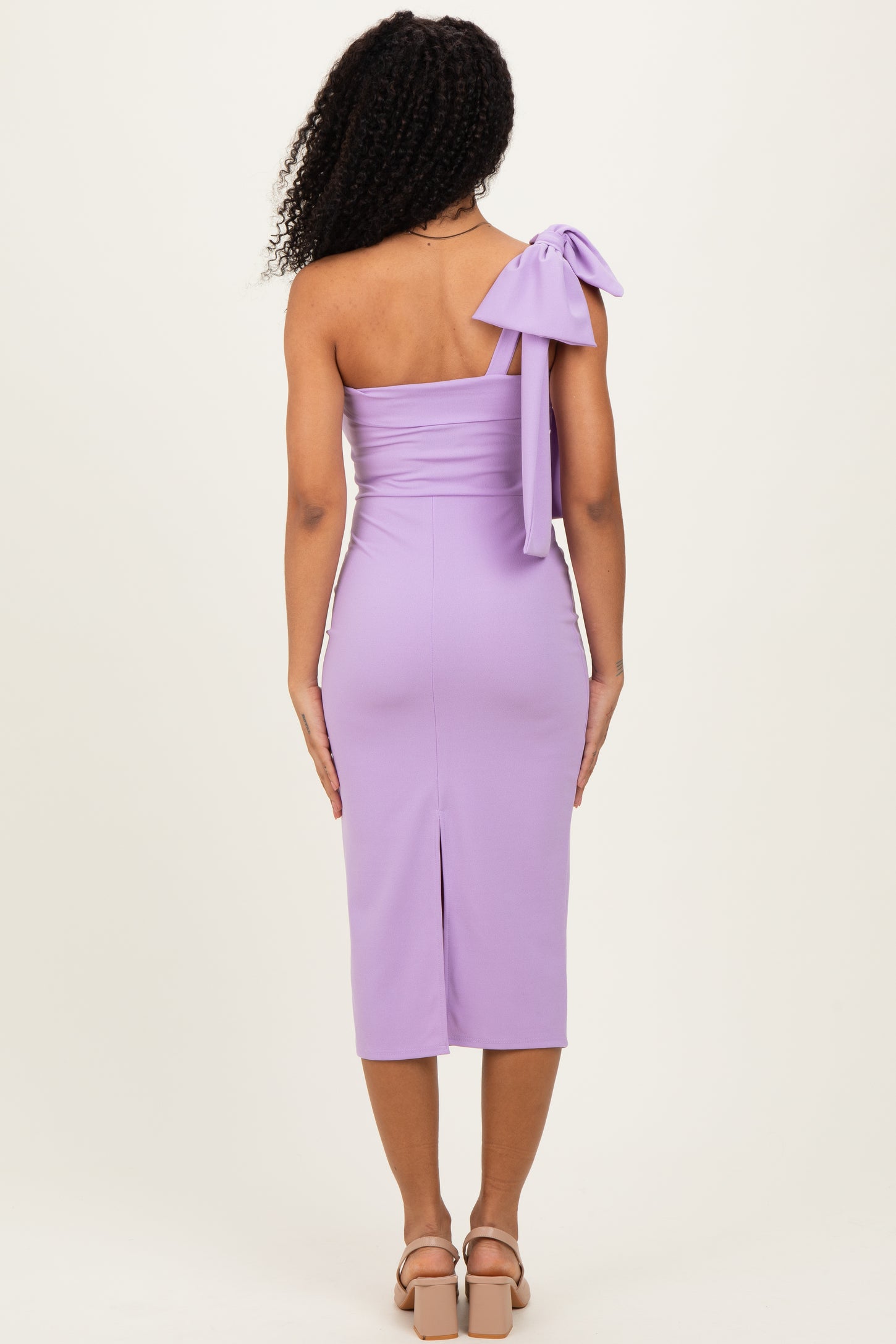 woman wearing a lavender one-shoulder dress with a bow detail on the shoulder and a slit at the back